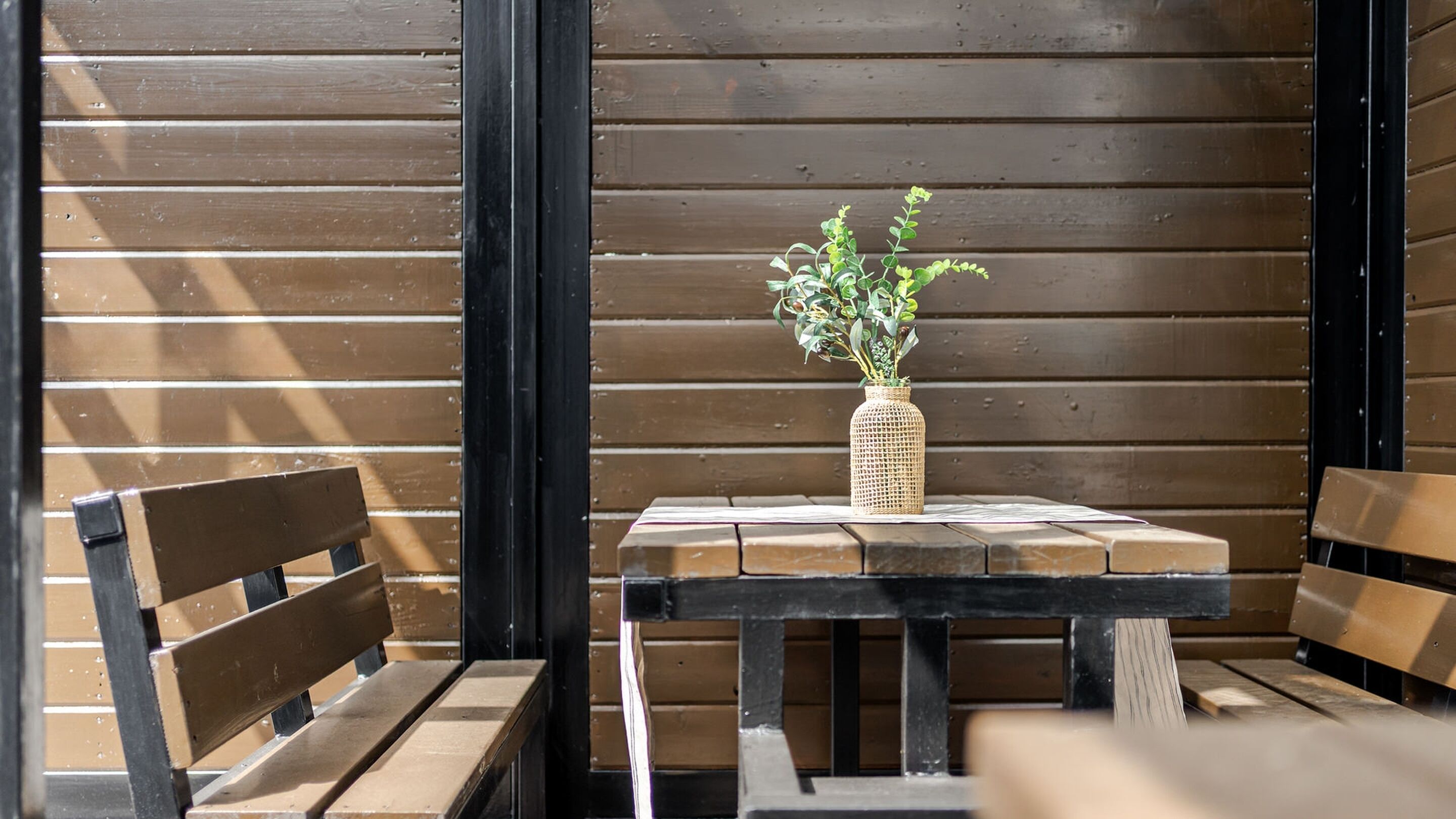 A wooden bench and table with a woven basket containing green plants.