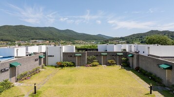 Un patio con un césped central, rodeado de edificios con unidades de aire acondicionado visibles, y montañas al fondo.