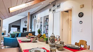 A dining area with a wooden table set for four, surrounded by bookshelves and a television in the background.