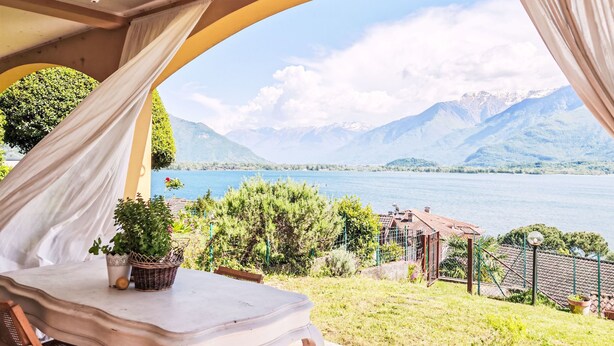 Eine Terrasse mit Tisch und Stühlen, Blick auf einen See und Berge im Hintergrund.