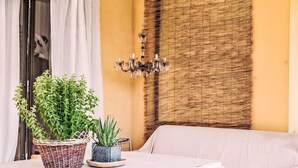 Ein Zimmer mit weißem Tisch, Korbwannen mit Pflanzen, einer Wandverkleidung aus Weide und einem weißen Sofa, sowie einer Kristallleuchter.