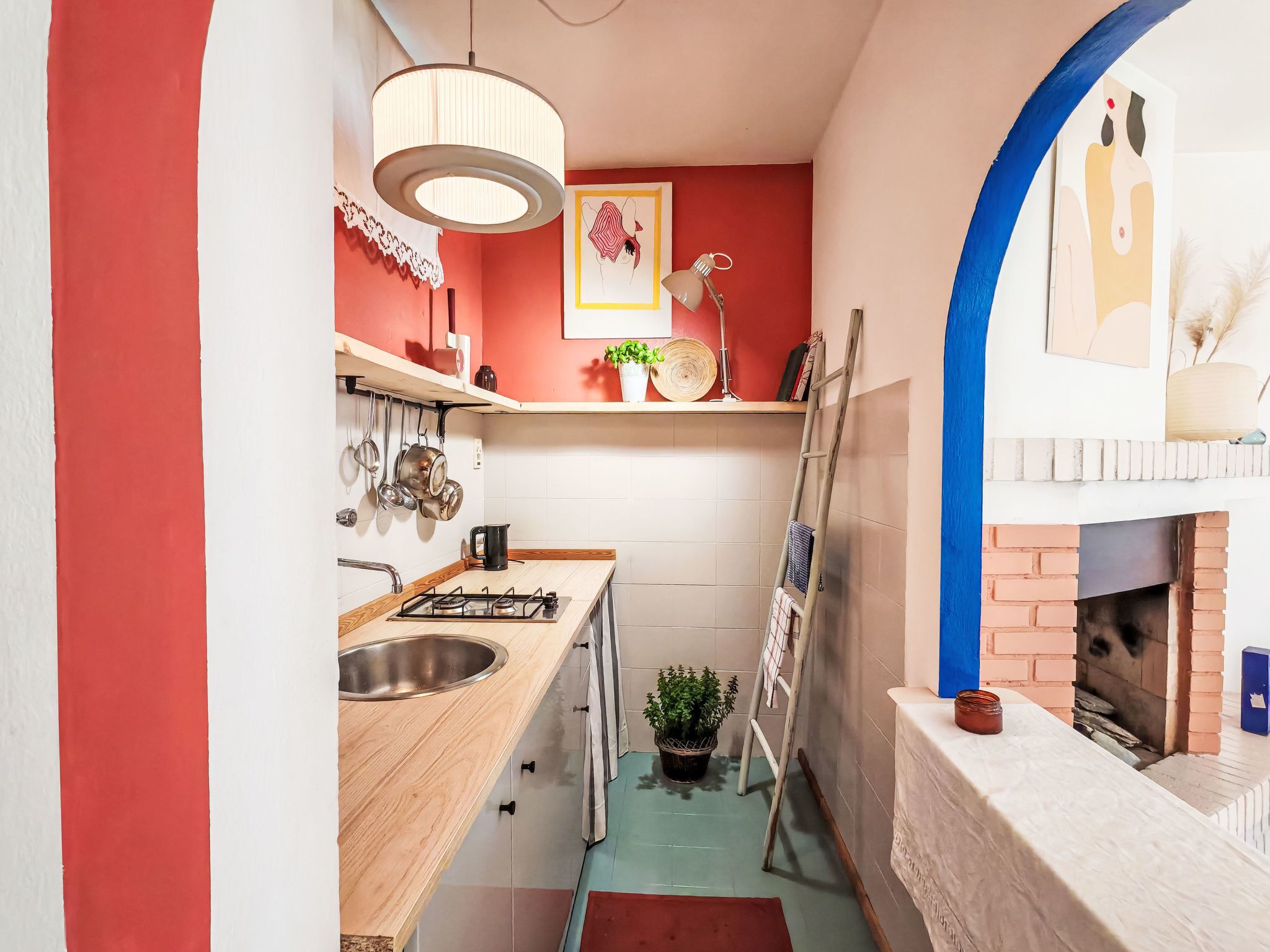 A narrow kitchen with a gas stove, a sink, and a brick fireplace.