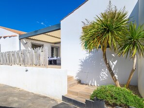 Een modern huis met een terras, een houten schutting en een palmboom.