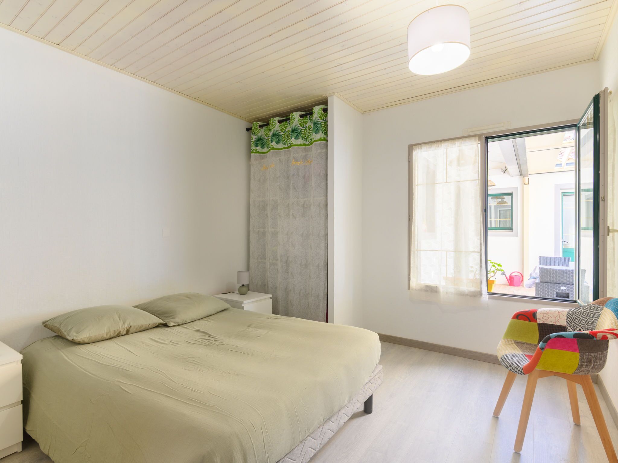 A bedroom with a bed, a nightstand, a window with a view, and a chair.