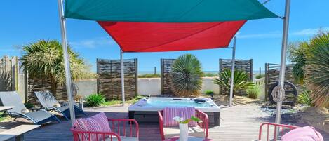 A wooden deck with outdoor seating, a hot tub, and a large canopy providing shade.