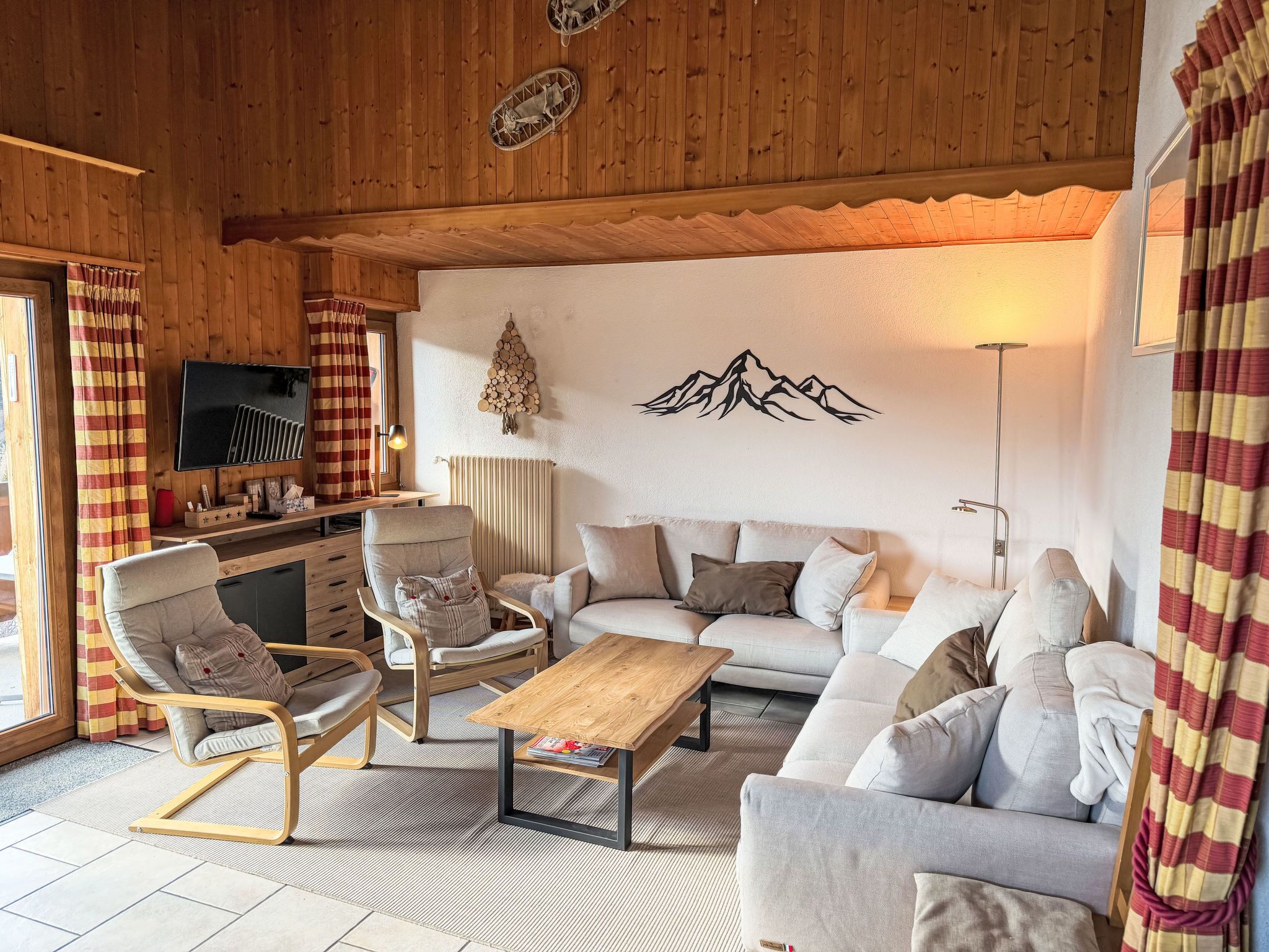 Una sala de estar acogedora con techo de madera, un conjunto de sofás, una mesa de centro, un televisor y una decoración en la pared.