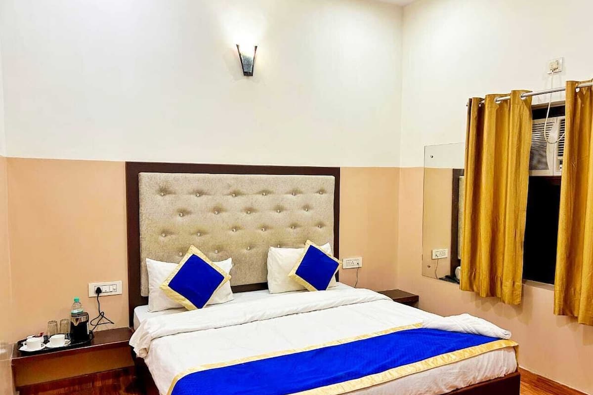 A hotel room with a large bed, a nightstand, a wall-mounted light, and a window with curtains.