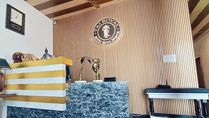A reception area with a marble counter, a clock, and a wall with vertical wooden slats and a logo. - Hotel Taj Royal (Agra)