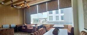 Un restaurant moderne avec de hauts plafonds, un plafond orné de motifs et de grandes fenêtres donnant sur les bâtiments environnants.