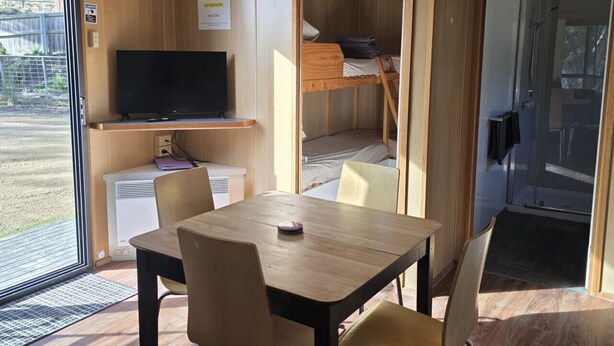 Una habitación compacta con una mesa de madera, sillas, televisor y una cama litera.