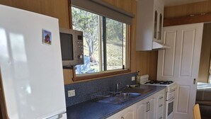 Una cocina compacta con armarios blancos, encimera azul, estufa integrada y ventana con vistas a un paisaje natural.