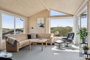A modern living room with a sofa, coffee table, and armchair, large windows, and a view of the landscape.