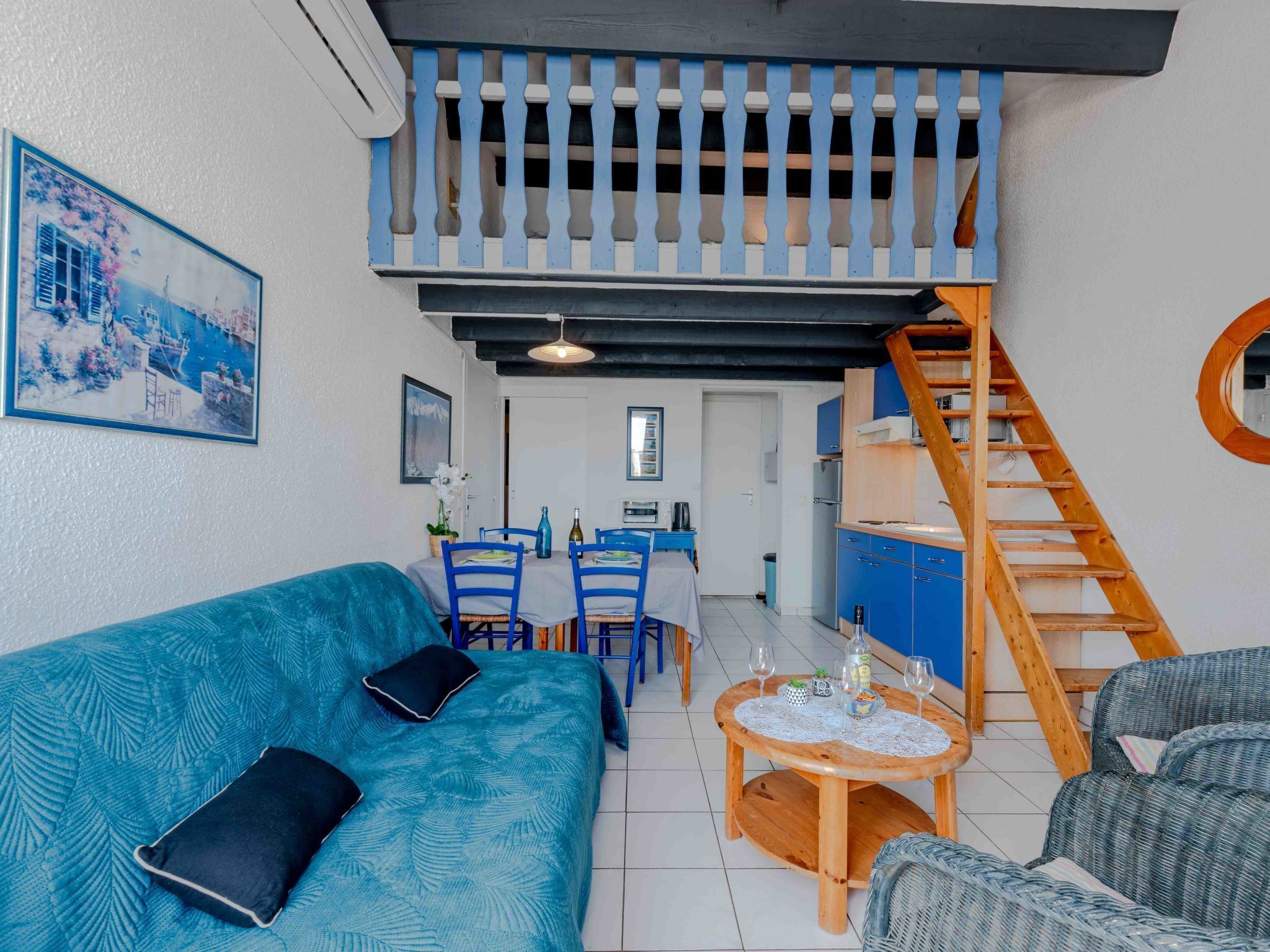 A cozy living room with a blue sofa, a wooden table, and a staircase leading to a kitchen area.