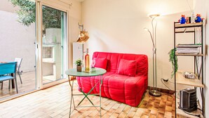 Una habitación con un sofá rojo, una pequeña mesa redonda, una lámpara de pie y una estantería.
