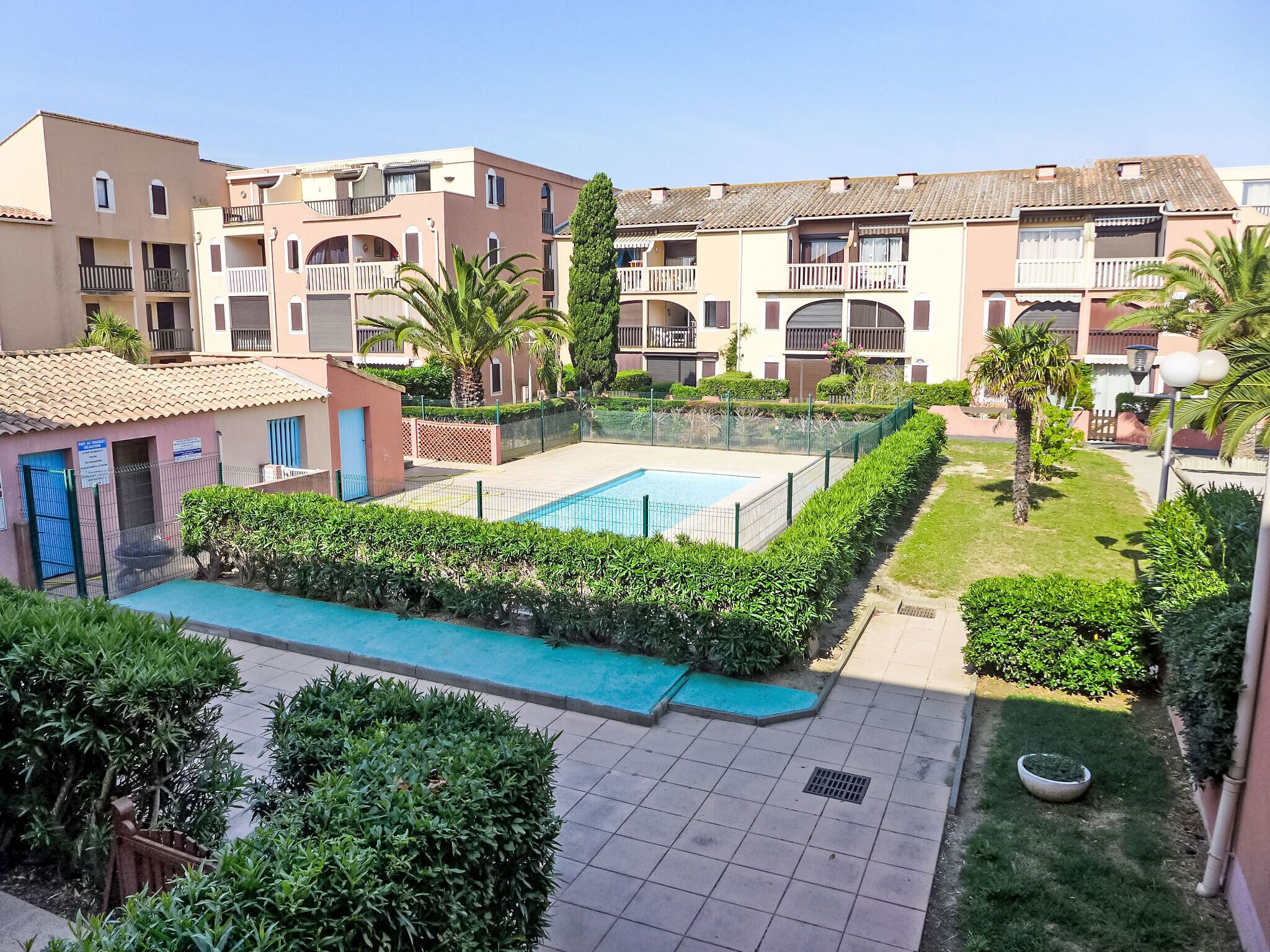 A residential building with a swimming pool surrounded by greenery and a small garden area.
