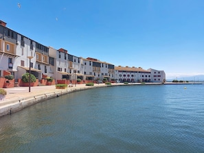 A waterfront building with balconies, a paved walkway, and a calm water body.