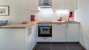 A modern kitchen with white cabinets, a stainless steel range hood, a red coffee maker, a sink, and a basket with kitchen towels. - Simonhöhe by Interhome (Sankt Urban)