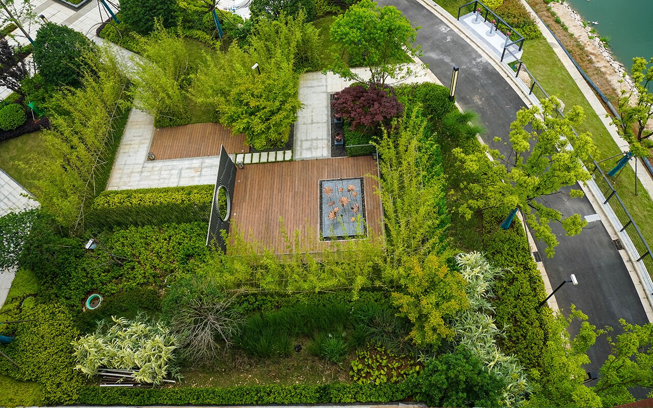 Vista aérea de uma área ajardinada com um deck de madeira, um mural e diversos tipos de vegetação.
