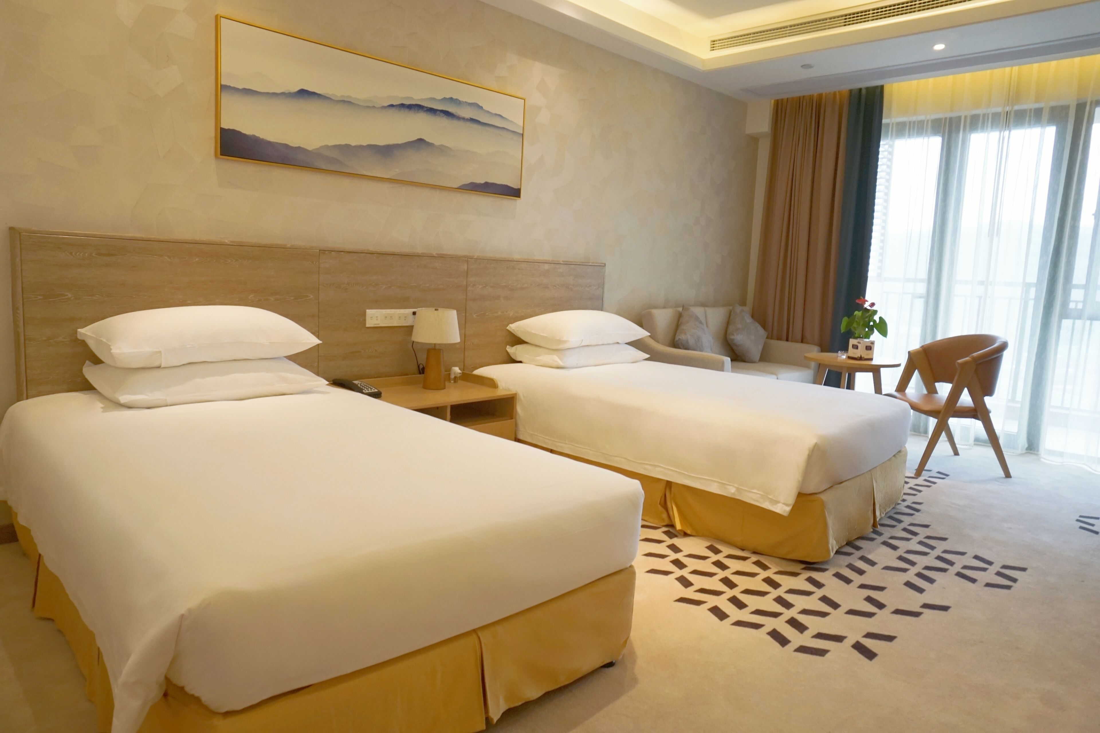 A hotel room with two beds, a sofa, a chair, a lamp, and a painting on the wall.