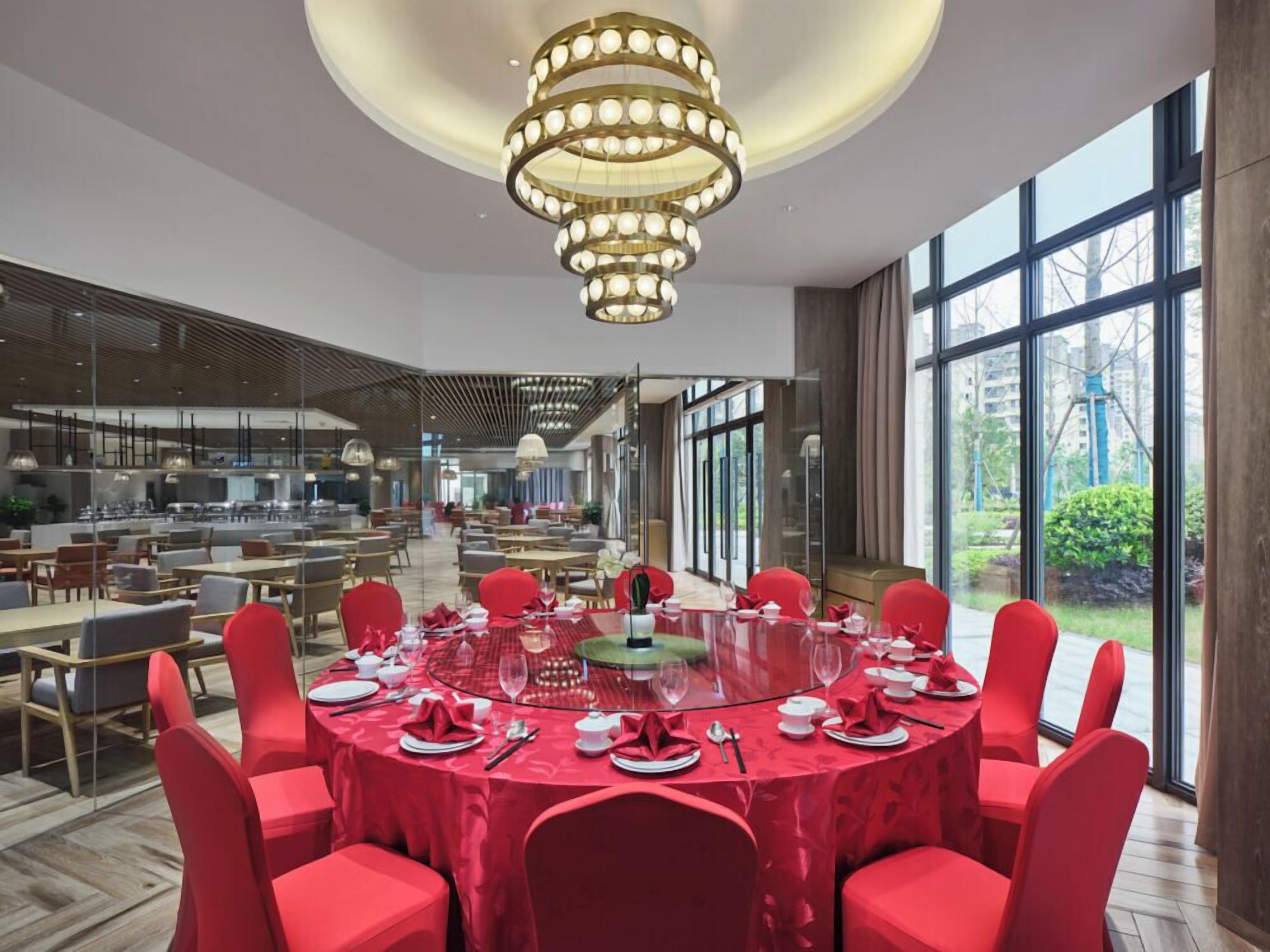 A spacious dining area with round tables, red chairs, and a modern chandelier.