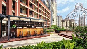 A modern building with multiple balconies, a bar area with stools, and a well-maintained garden. - Q-Box Hotel Hangzhou Bay Ningbo (Ningbo)