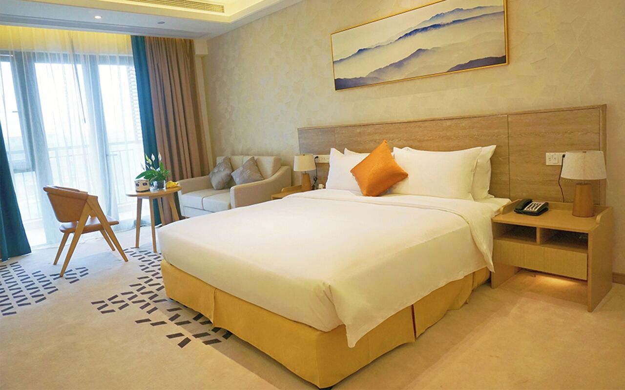 A hotel room with a large bed, a sofa, a small table, and a lamp.