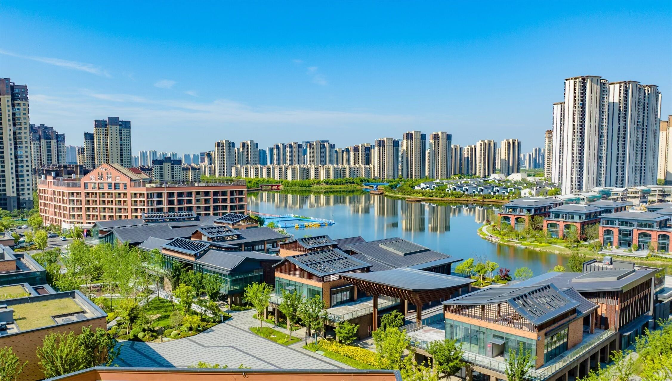 Un moderno complejo hotelero con varias edificaciones, un río al fondo y el horizonte de una ciudad.