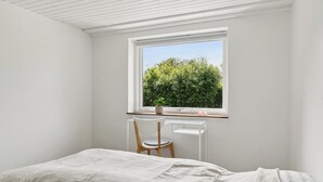 A bedroom with a bed, a desk with a chair, and a window with a view of greenery. - Lovely cottage, close to beach and forest (Nakskov)