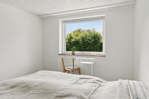 A bedroom with a bed, a desk with a chair, and a window with a view of greenery.