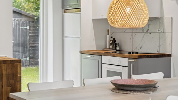 A modern kitchen with white cabinets, a wooden countertop, and a hanging pendant light. - Lovely cottage, close to beach and forest (Nakskov)