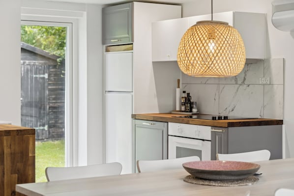 A modern kitchen with white cabinets, a wooden countertop, and a hanging pendant light.
