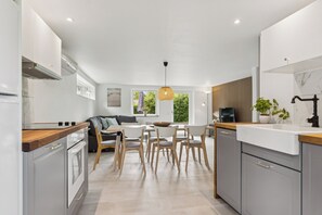 A modern kitchen with white cabinets, a wooden countertop, and a dining area with chairs and a table.