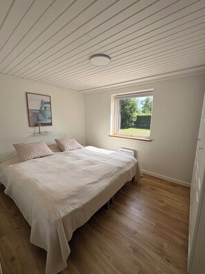 A bedroom with a bed, a window, a radiator, and a ceiling light. - Lovely cottage, close to beach and forest (Nakskov)