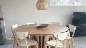 A round dining table with six chairs, a woven pendant light, and a flat-screen TV in a modern interior. - Lovely cottage, close to beach and forest (Nakskov)