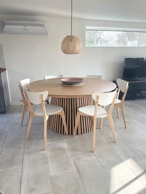 A round dining table with six chairs, a woven pendant light, and a flat-screen TV in a modern interior. - Lovely cottage, close to beach and forest (Nakskov)