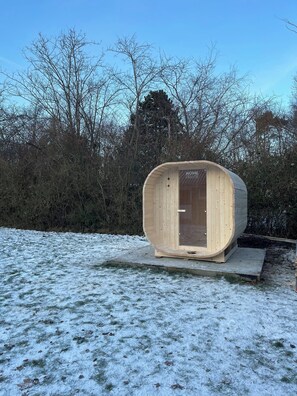 A wooden sauna structure with a door, surrounded by snow-covered ground and leafless trees. - Lovely cottage, close to beach and forest (Nakskov)