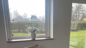 A room with a large window, a wooden chair with a furry cushion, and a potted plant on the windowsill. - Lovely cottage, close to beach and forest (Nakskov)