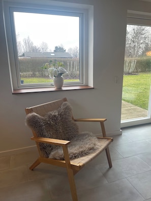 A room with a large window, a wooden chair with a furry cushion, and a potted plant on the windowsill.
