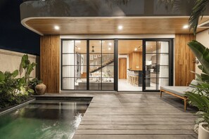 Een modern huis met een zwembad, een houten terras en een grote glazen deur die leidt naar een woonruimte met een trap.