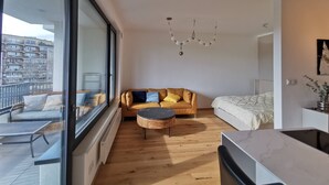 A modern apartment with a large window, a sofa, a round coffee table, a bed, and a kitchen area. - free Parking, center location, Nuslesky Pivovar sunset balcony home (Hlavní město Praha)