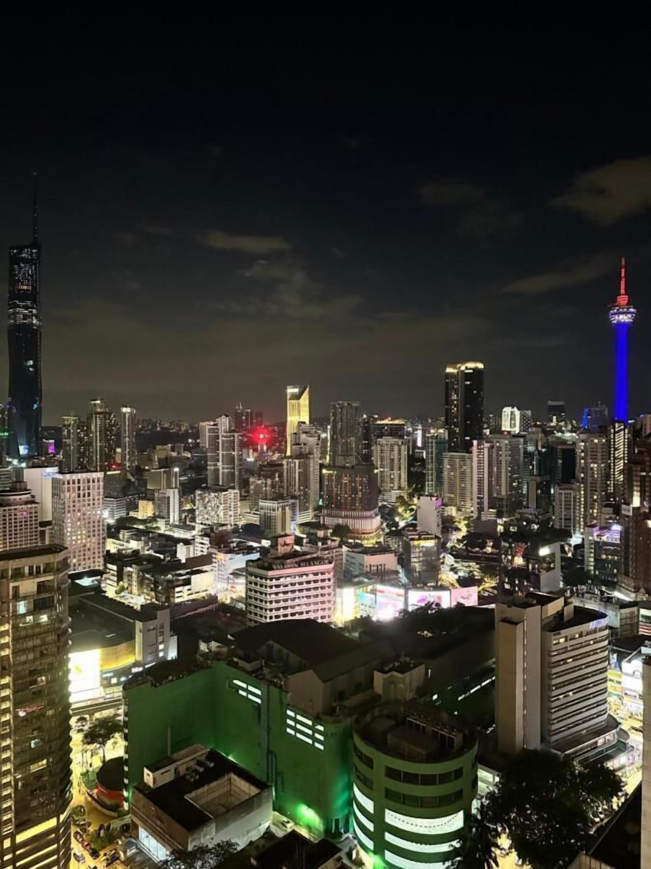 A nighttime cityscape with illuminated buildings and a prominent tower with red and blue lights.
