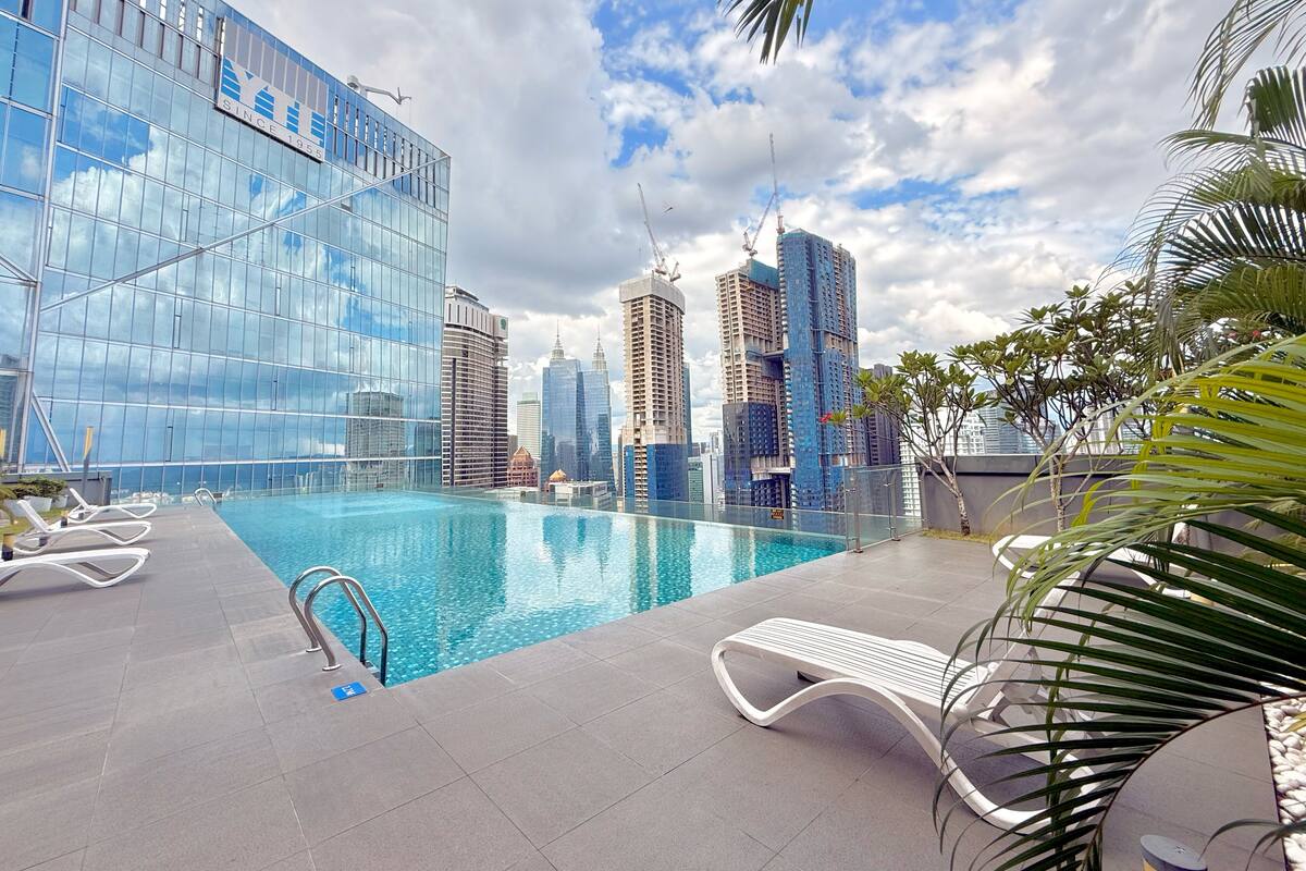 Ein Pool auf dem Dach mit Liegestühlen, umgeben von modernen Gebäuden und Palmen.