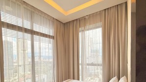 Une chambre d’hôtel moderne avec un grand lit, des rideaux de couleur beige et une vue sur la ville.