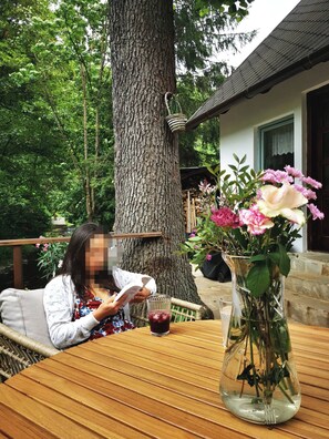 Una persona leyendo un libro en una mesa de madera, con un vaso de bebida roja y un florero con flores.