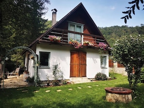 A two-story house with a sloped roof, wooden balcony with flower boxes, and a stone staircase leading to the entrance.