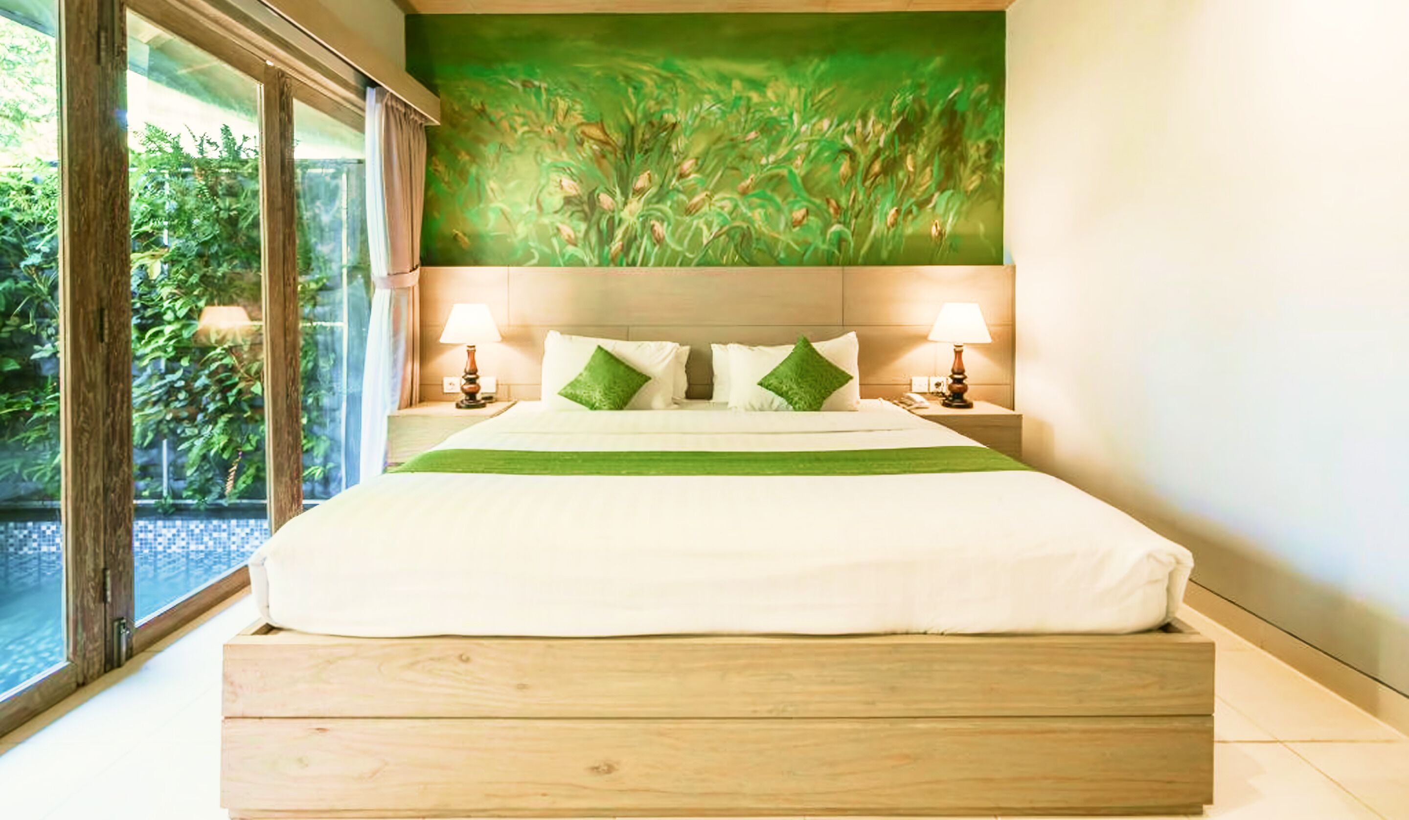 Un grand lit avec une structure en bois, deux tables de chevet avec des lampes, une fresque murale verte et une vue sur la verdure par une grande fenêtre.