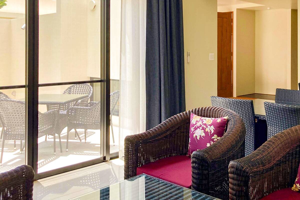 A room with wicker furniture, a glass table, and a view through a large window.