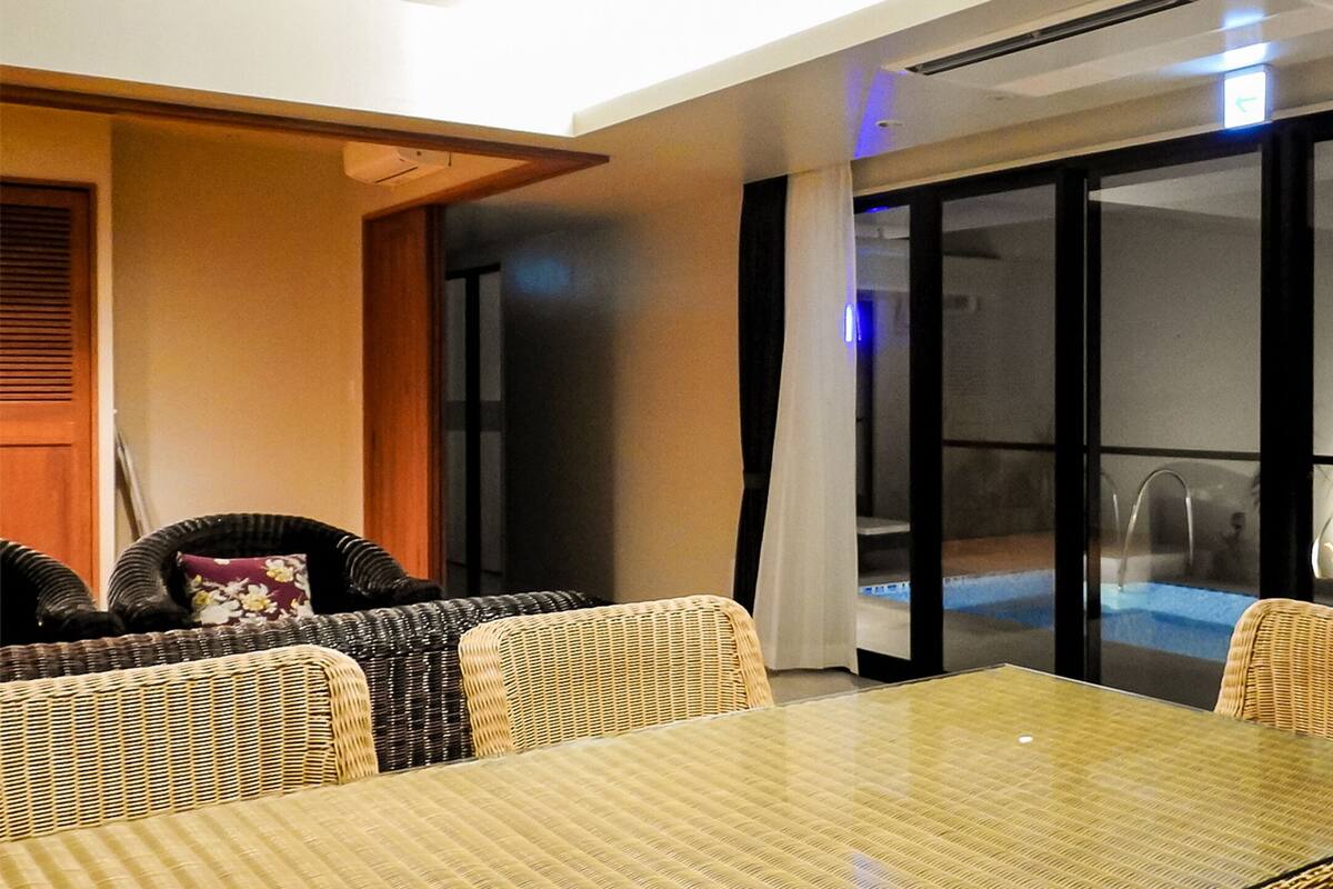 A room with a glass table and wicker chairs, a sliding glass door leading to a pool, and a ceiling fan.