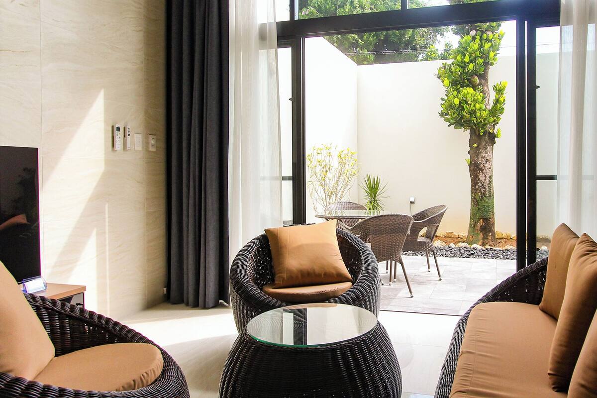 A modern living room with wicker furniture, a glass coffee table, and a view of an outdoor patio area.