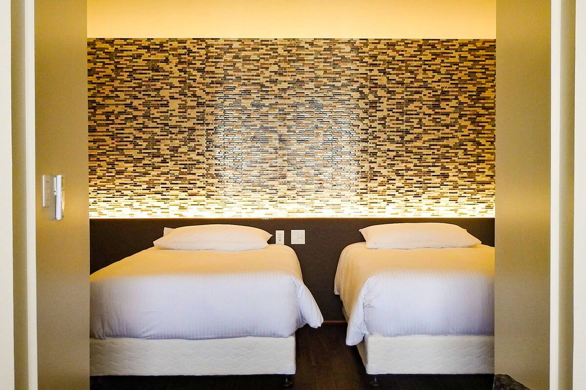 A room with two beds, a wall with a mosaic pattern, and a light fixture above the beds.